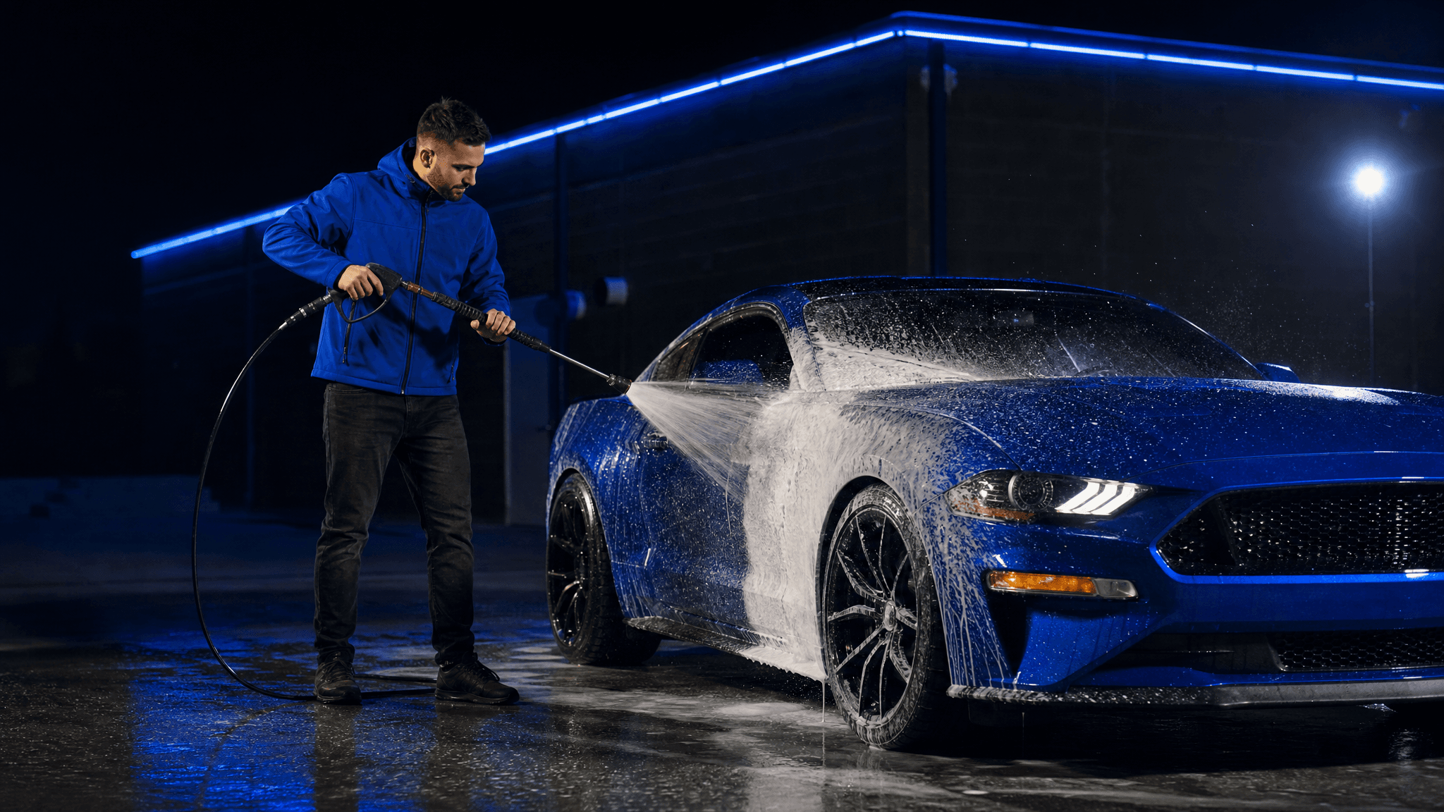 Surf Thru team member spraying down a glossy blue car at night